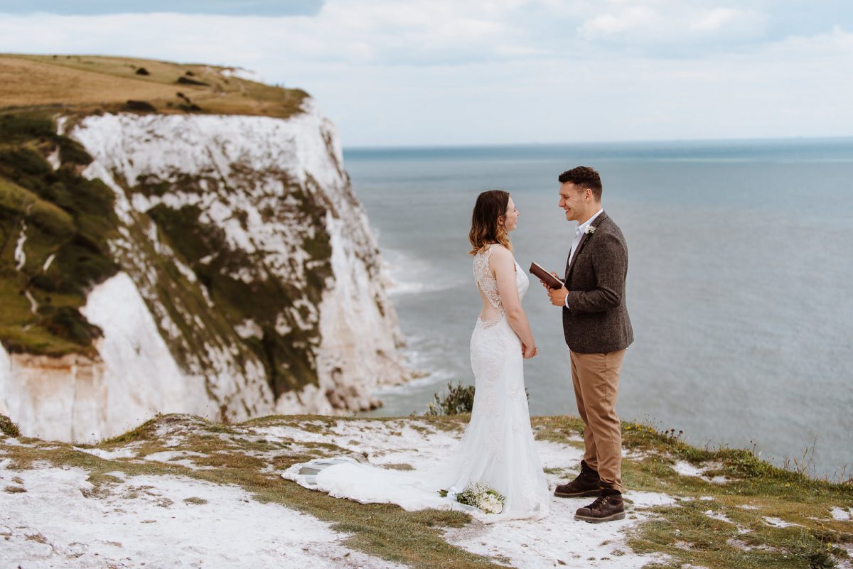 Couple having their elopement ceremony on a cliff. The groom is reading his vows for the bride.
