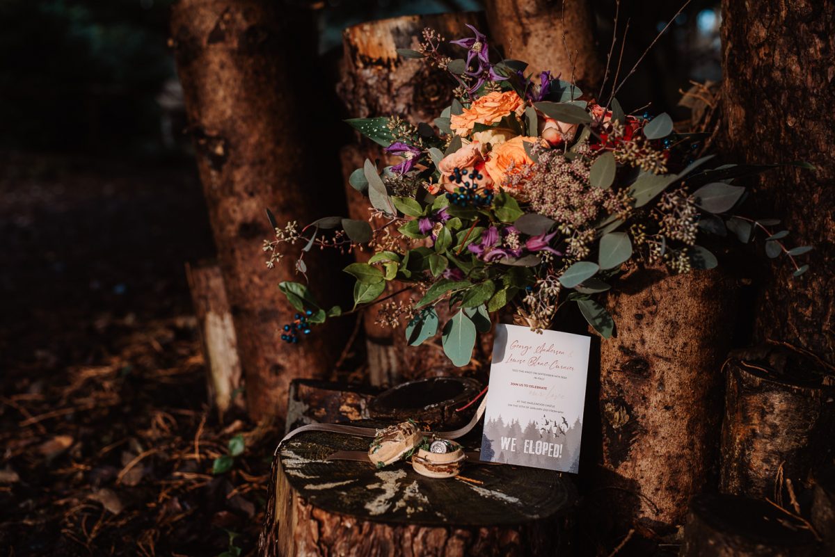Picture showing wedding details. A wild flowers bouquet with orange tones, a wooden rings box, and an elopement announcement card