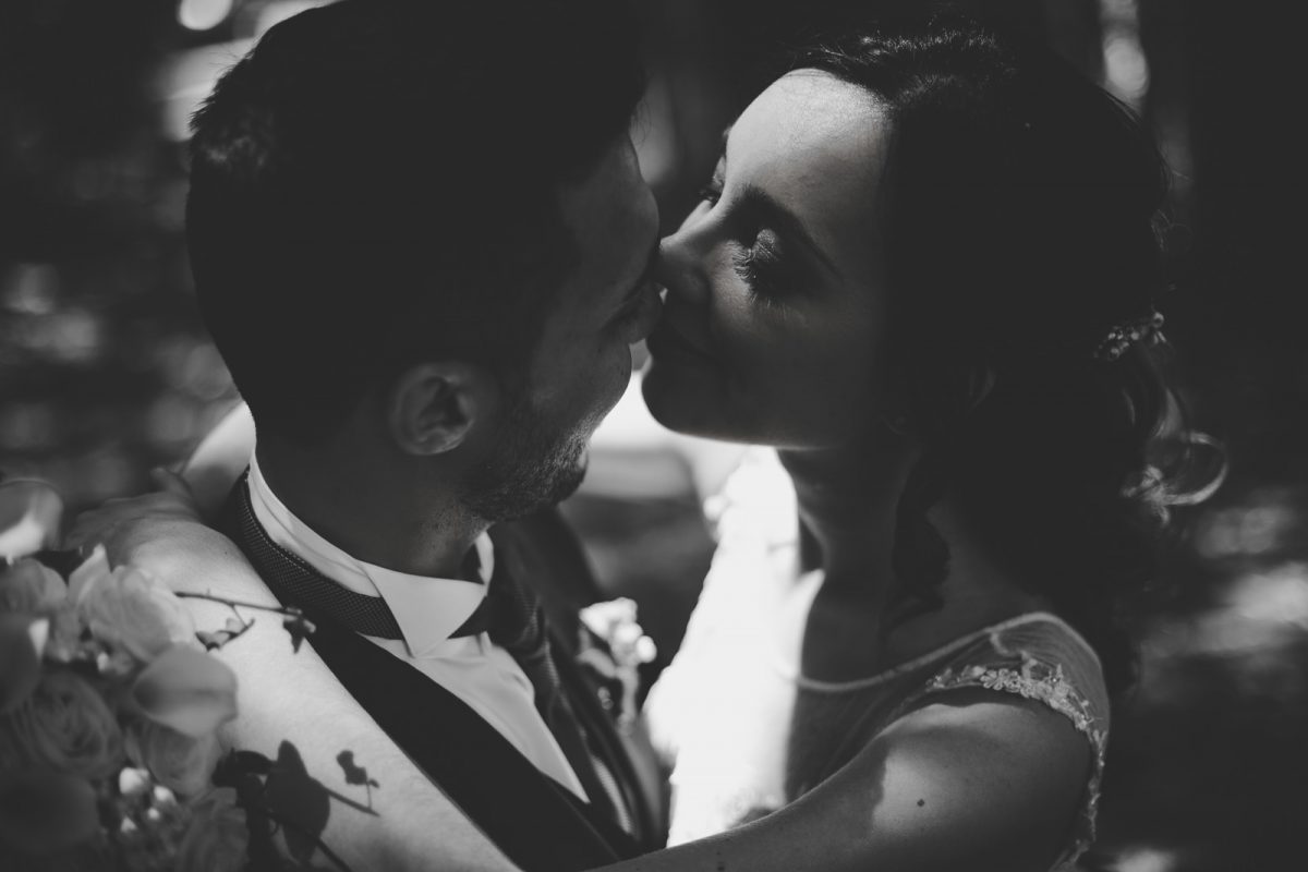 A black and white portrait of a just married couple. The bride is gently rubbing her face to the groom face