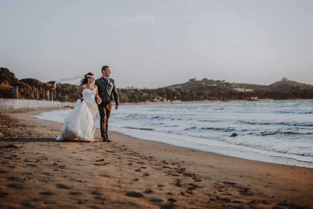 Beach elopement in Tuscany. Couple walking on the beach looking at the sunset.