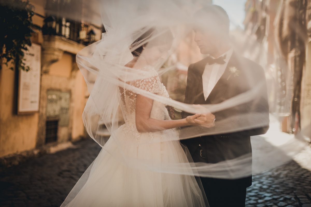 Bride and groom in Trastevere Rome. The bride is close to the groom, and the veil is moving around her.