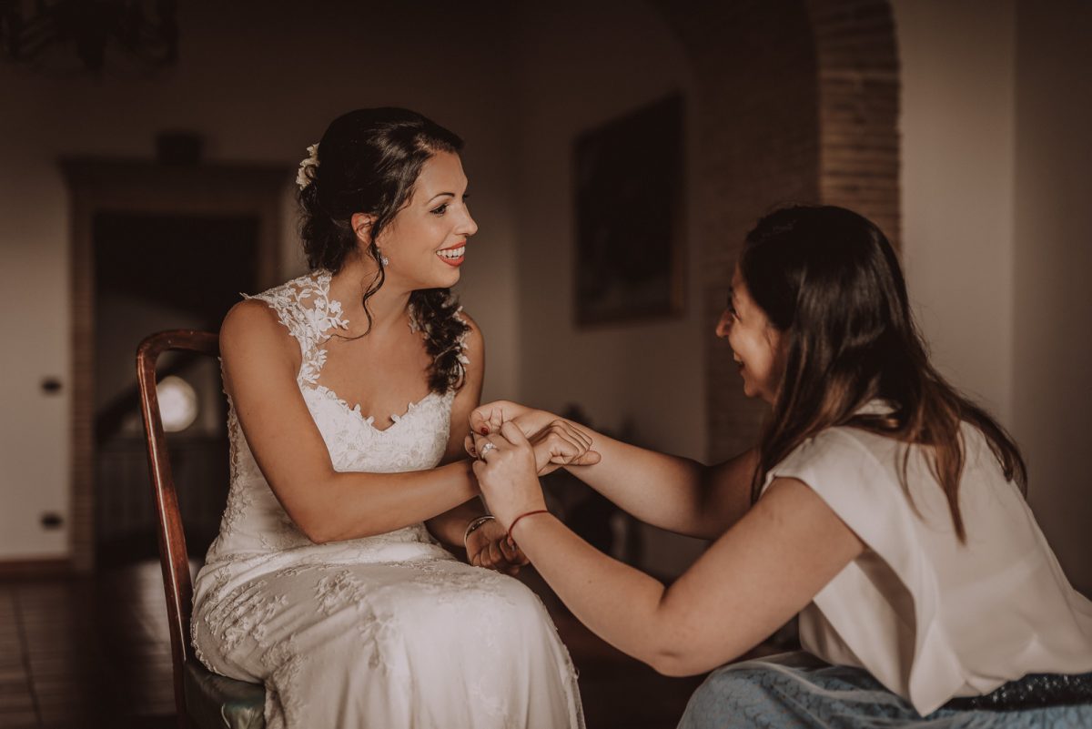 Bride getting ready before the ceremony. Friend is helping her with the bracelet.