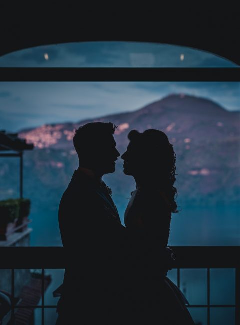 Portrait of a couple facing each other in front of a window. It is almost dark, there is a mountain in the background.